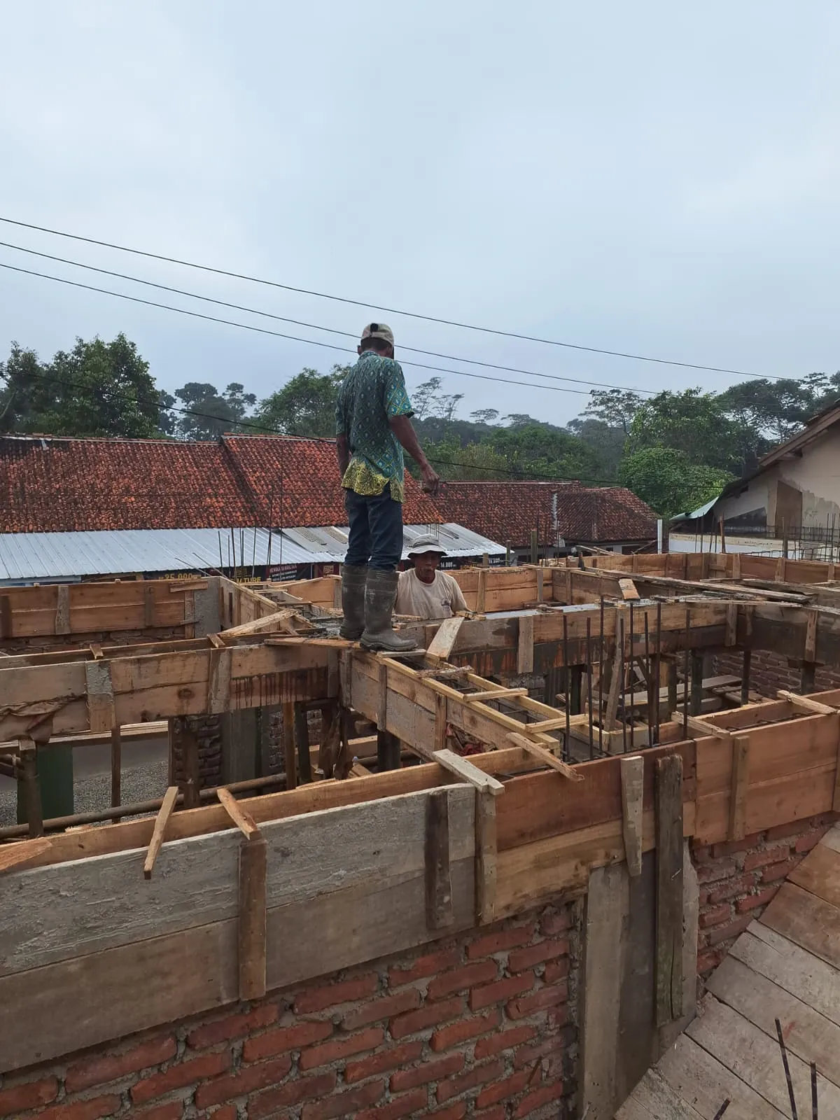 Pekerja memasang bekisting ring balok di atas dinding bata